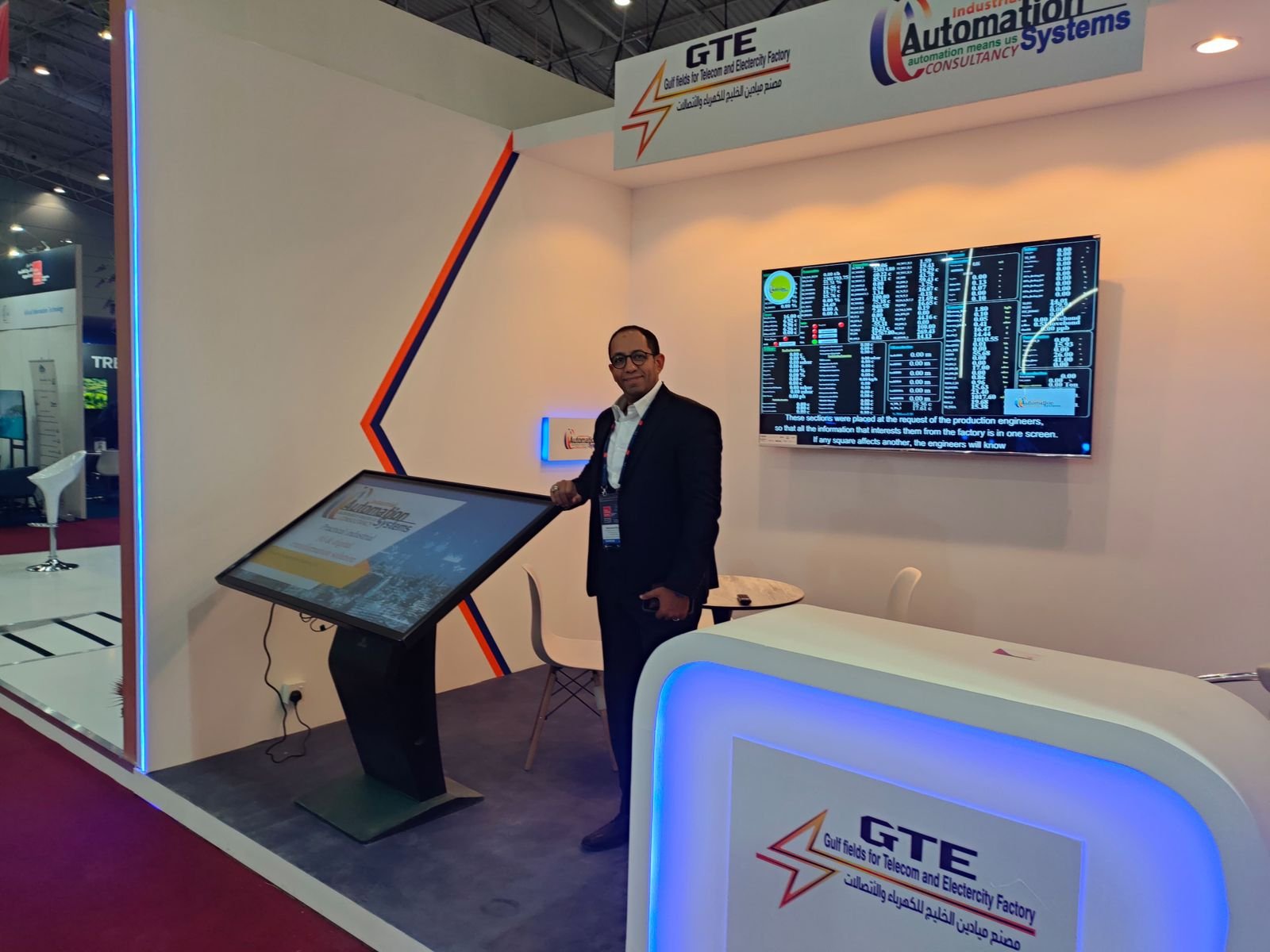 Company representative showcasing industrial automation systems and electrical panel solutions at an exhibition booth ممثل شركة متخصصة في تصنيع اللوحات الكهربائية وحلول الأتمتة يعرض أنظمة صناعية متقدمة داخل جناح المعرض